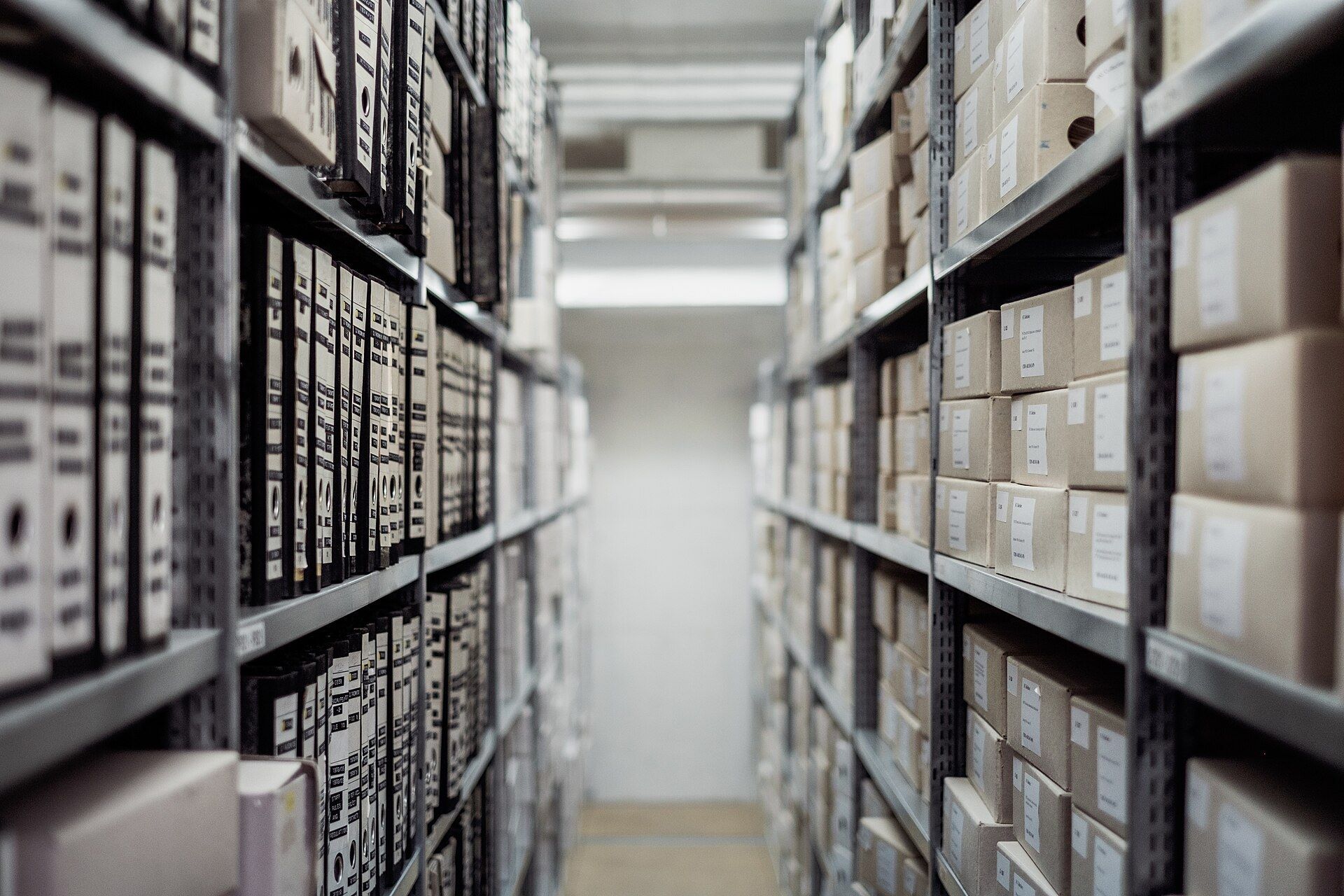 Rows of labeled boxes and folders on archive shelves. A Wikimedia Commons photograph on Brent O'Mara Insights.
