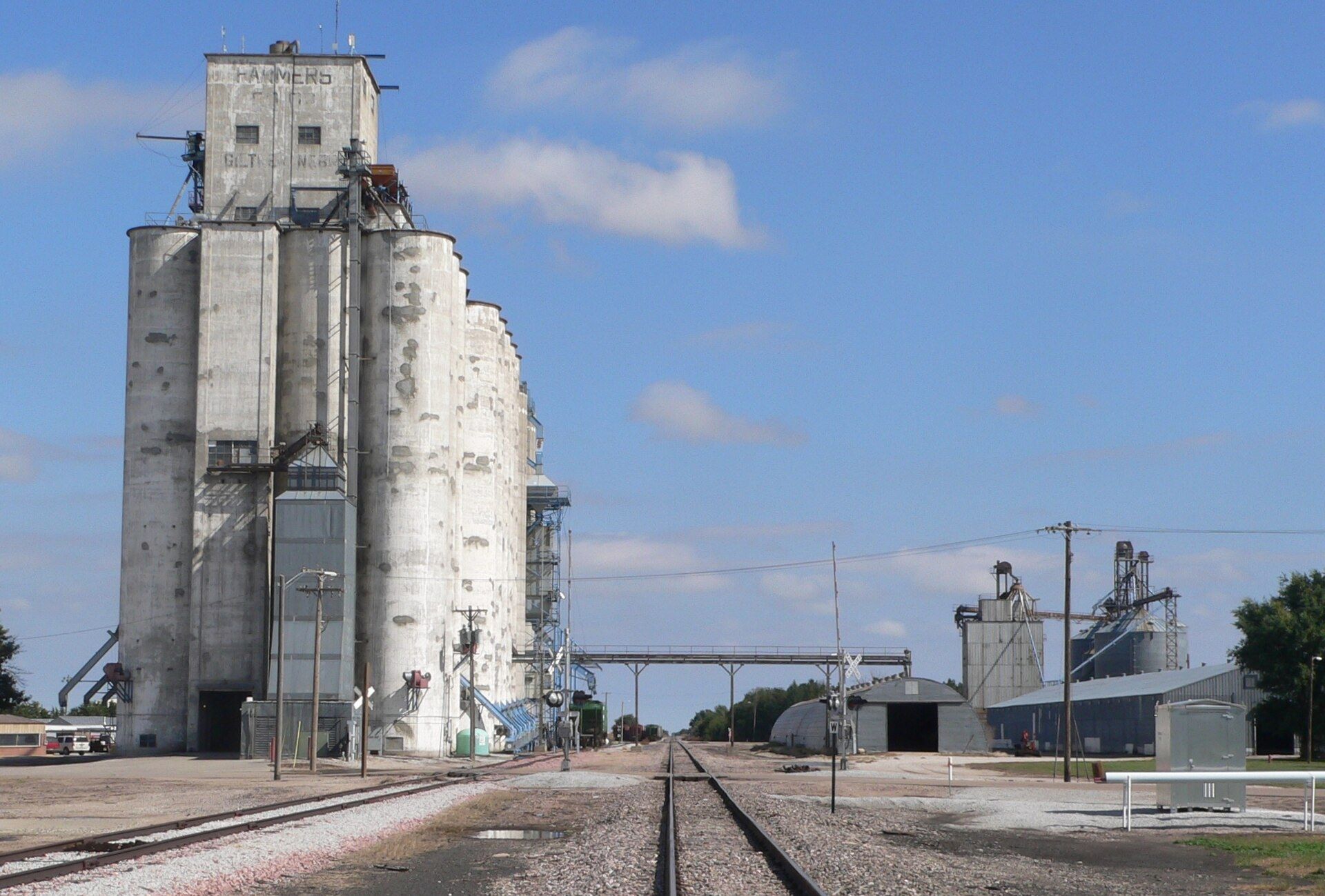 A concrete grain elevator rises above a small Nebraska town beside the rail line. A Wikimedia Commons photograph on Brent O'Mara Insights.